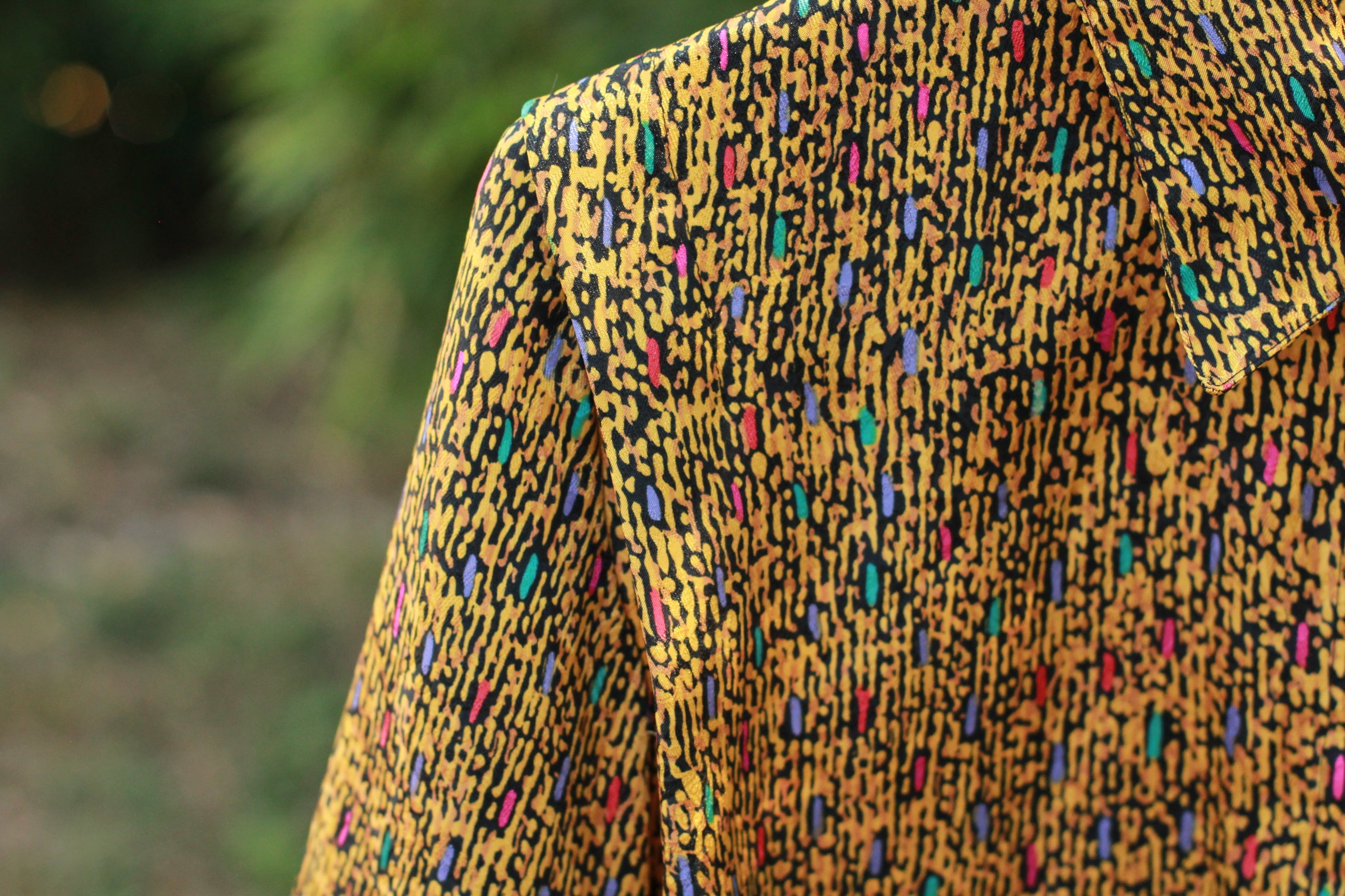 Textile close-up showing gold and black retro abstract print on polyester fabric.