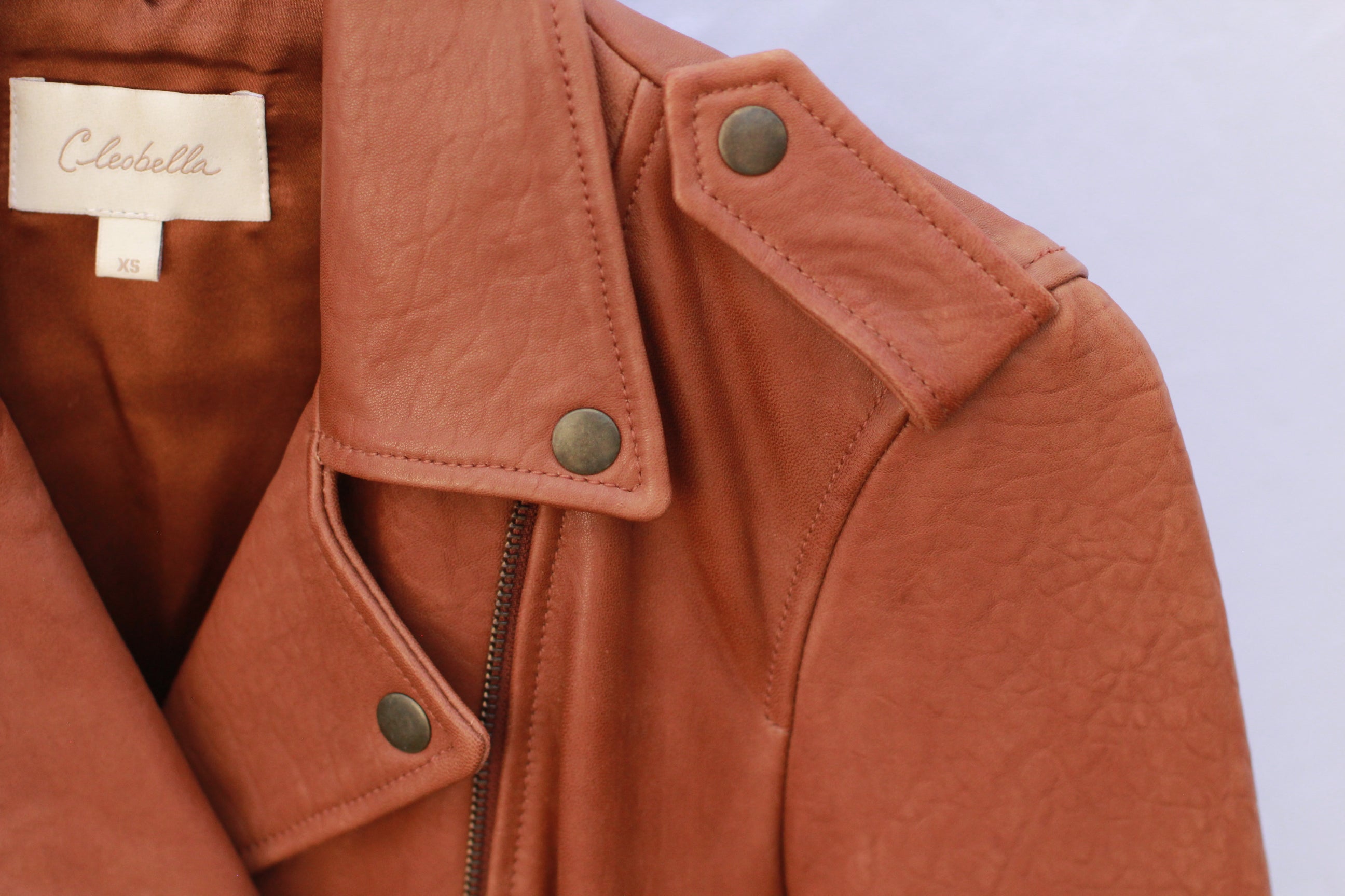 Close-up of brass hardware and asymmetrical zip on cognac leather jacket